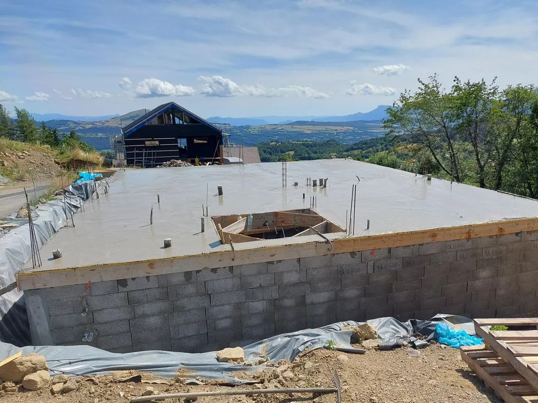 Dalle en béton armé fraîchement coulée sur un soubassement en parpaings, sommets des Hautes-Alpes en arrière-plan