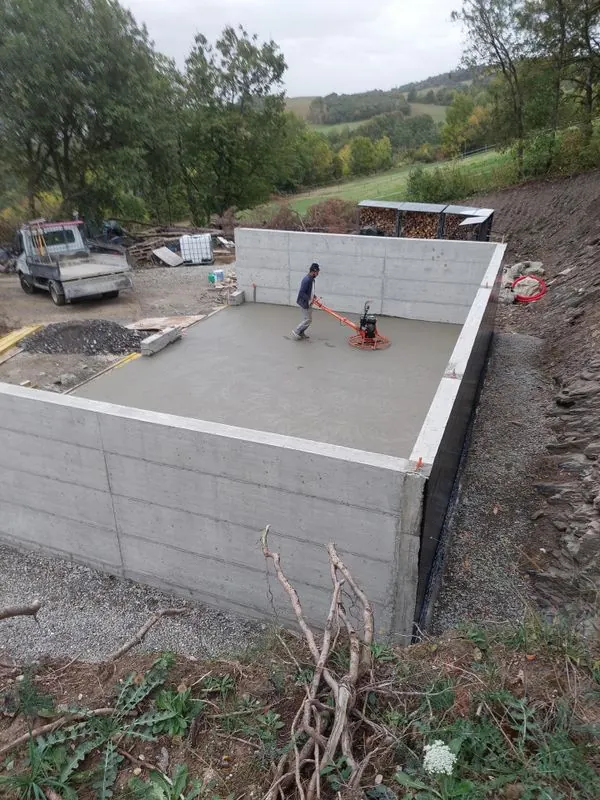 Ouvrier lissant une dalle de béton à la talocheuse mécanique, entre des murs en béton banché