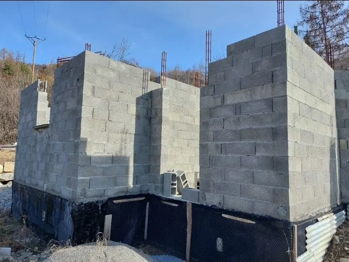 Murs en parpaings montés sur un soubassement protégé par une membrane, attentes de ferraillage en tête de mur