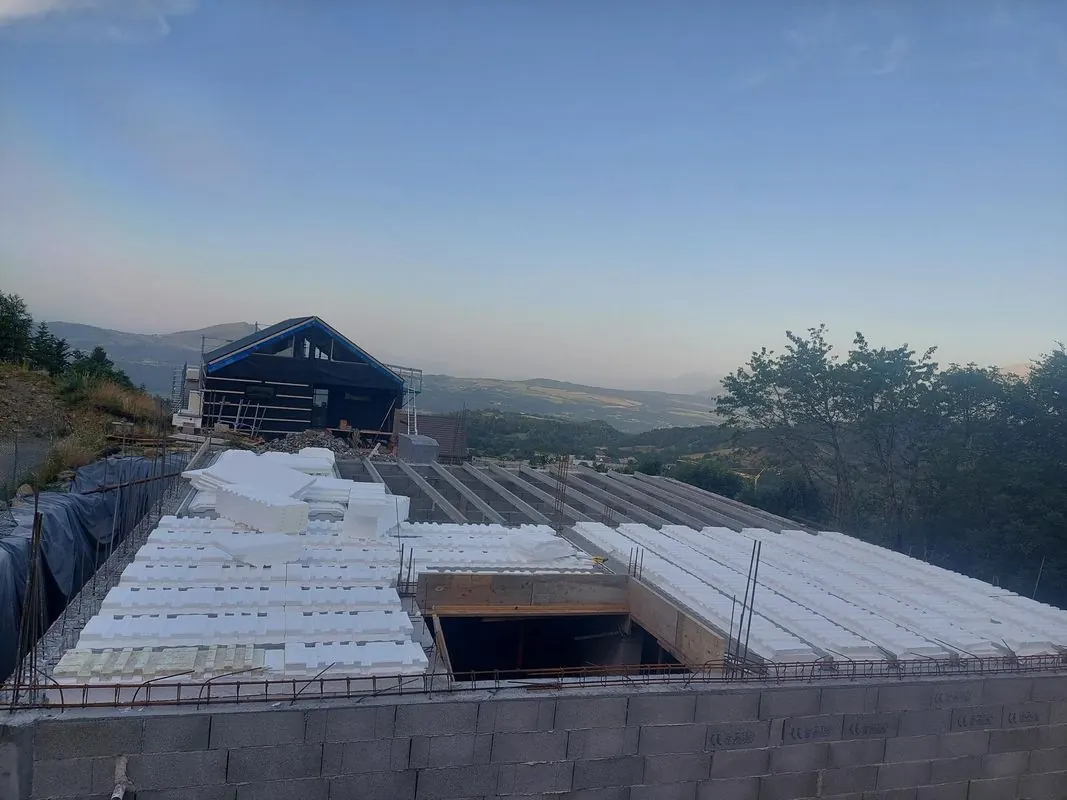 Plancher poutrelles-hourdis en cours de pose sur des murs en parpaings, avec les montagnes des Hautes-Alpes au loin